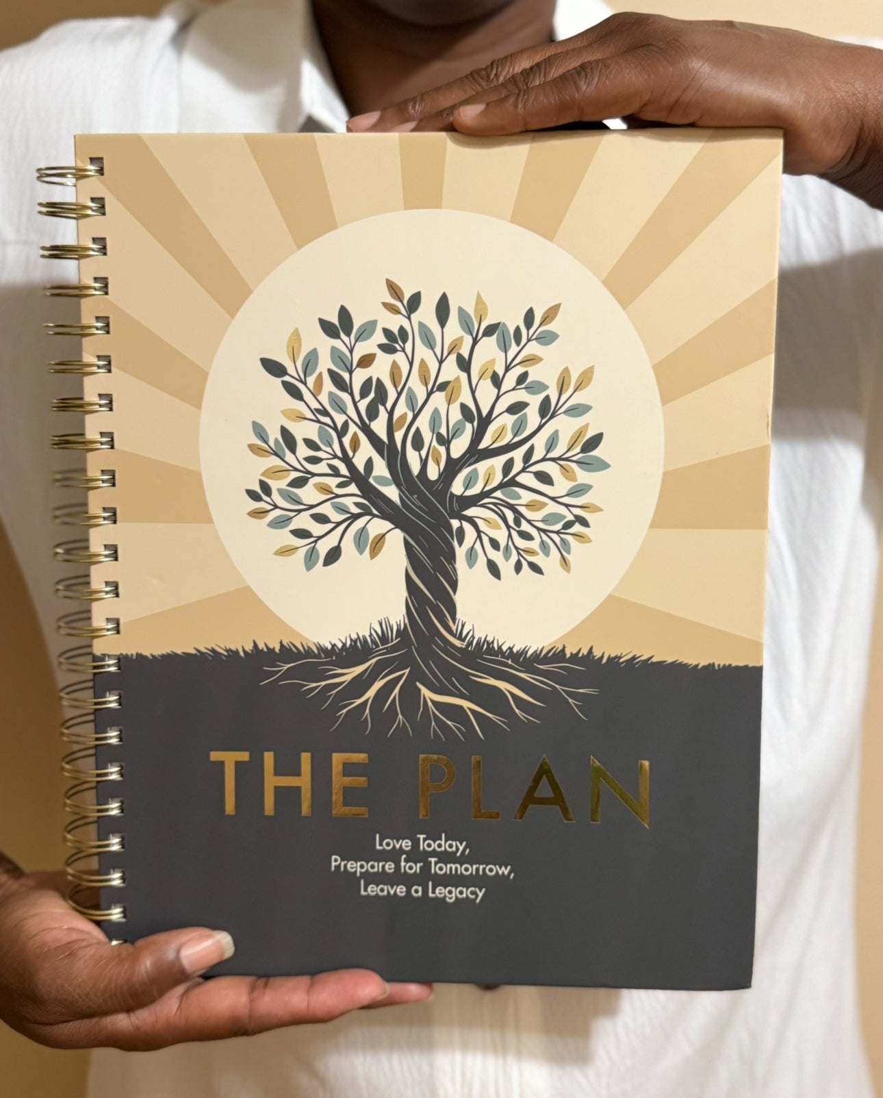 Planner titled 'The Plan' held by a person with a tree design on the cover.